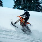 Snowmobile Trip - Side view of anonymous person in outerwear and helmet riding snowmobile on slope against coniferous trees on winter day