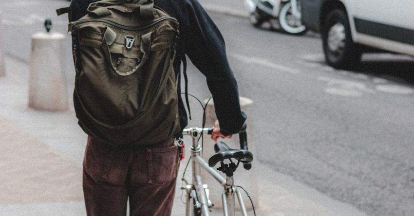 Cycling Tour - Full length back view of anonymous male traveler with backpack and cycle walking along asphalt road