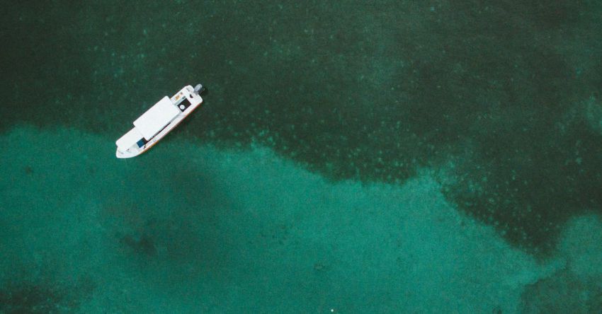 Fishing Trip - Drone view of white boat on surface of clear water with green algae on bottom