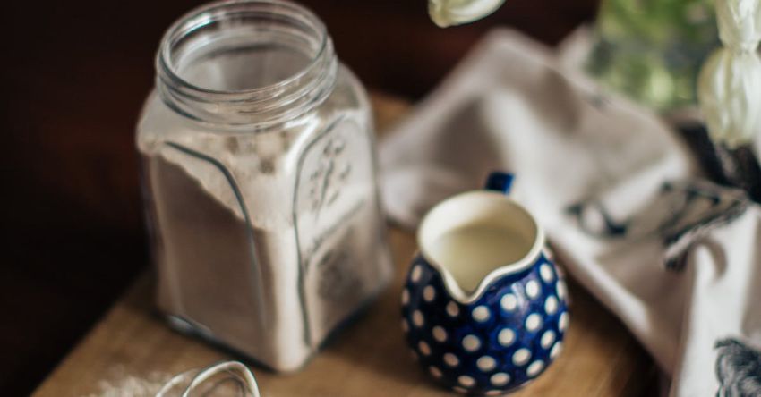 Cooking Equipment - From above of vase with white flowers placed near fresh milk eggs and glass jar with flour on cutting woody board at kitchen