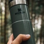 Hiking Equipment - A person holding a green thermos in the woods