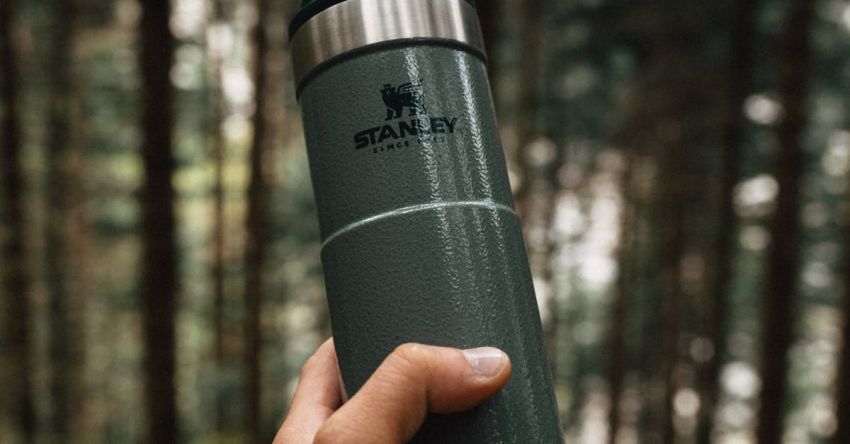 Hiking Equipment - A person holding a green thermos in the woods